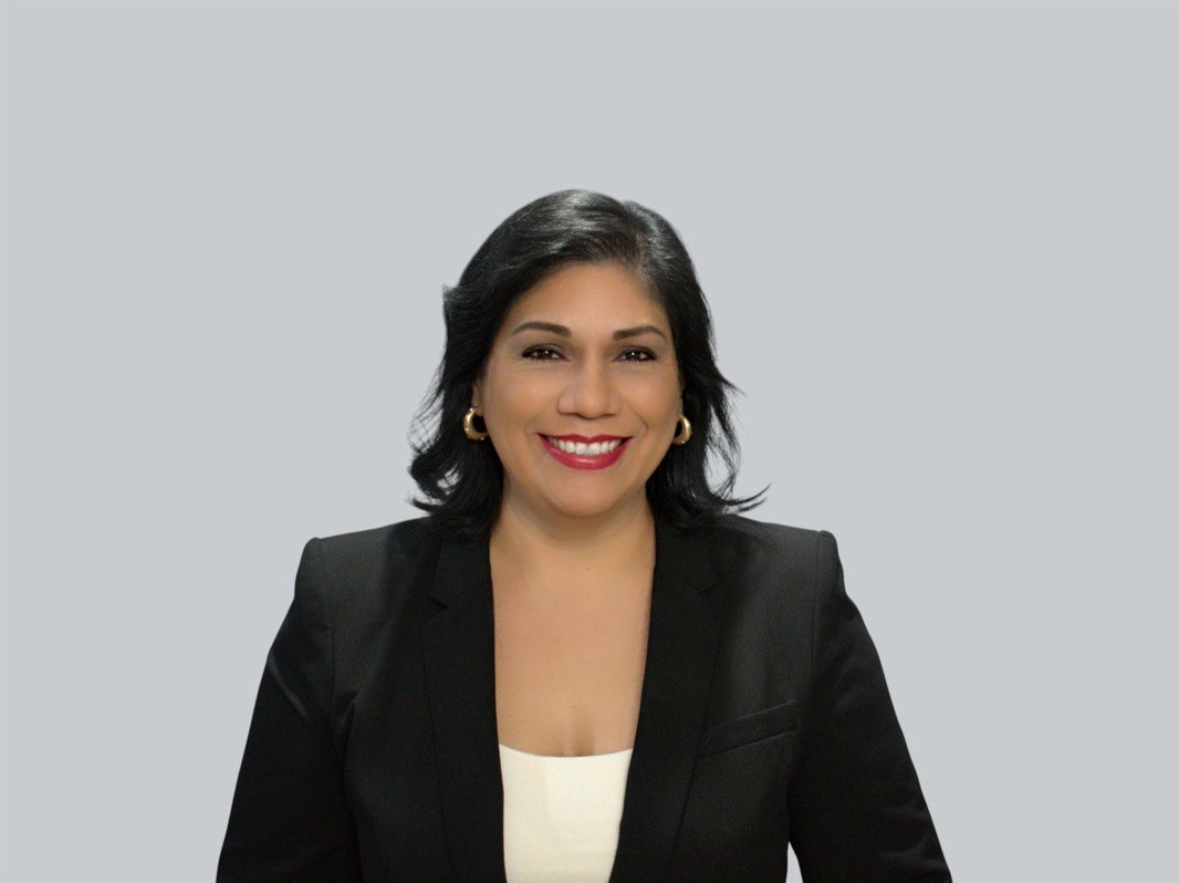 Smiling woman with dark hair in a black blazer and white top, posed against a plain gray background.